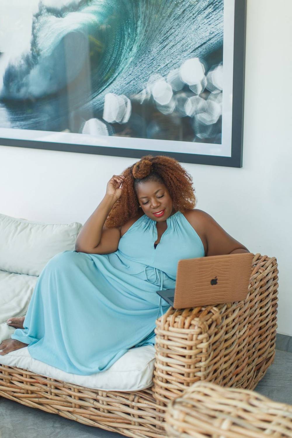 Kim McCarter in a light blue dress, lounging on a rattan sofa with her laptop